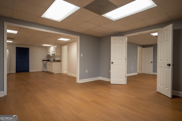 basement with freestanding refrigerator, a paneled ceiling, light wood-style flooring, and baseboards