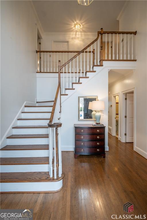 staircase featuring ornamental molding, baseboards, a towering ceiling, and hardwood / wood-style floors