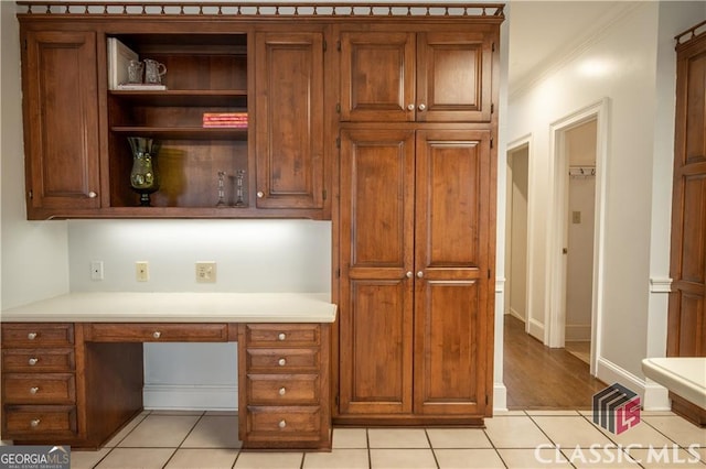 unfurnished office featuring baseboards, built in desk, light tile patterned flooring, and crown molding