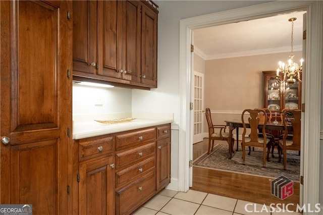 kitchen featuring light tile patterned floors, ornamental molding, brown cabinets, light countertops, and a notable chandelier