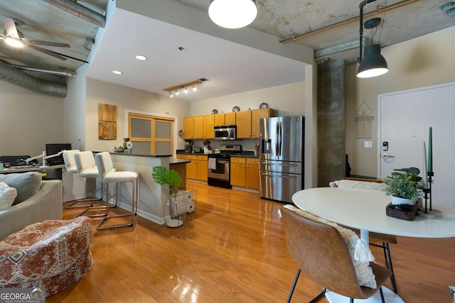 kitchen with stainless steel appliances, dark countertops, light wood-style flooring, a towering ceiling, and a peninsula