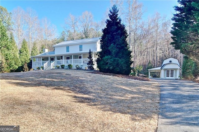 farmhouse-style home featuring a carport, covered porch, driveway, and a chimney