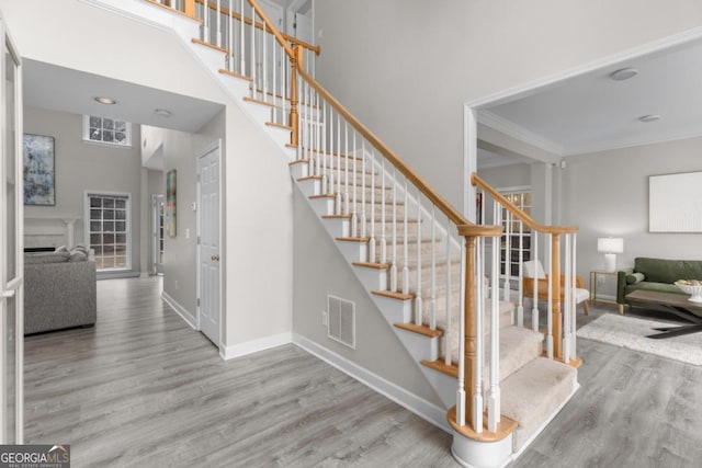 stairway with baseboards, visible vents, a towering ceiling, wood finished floors, and crown molding