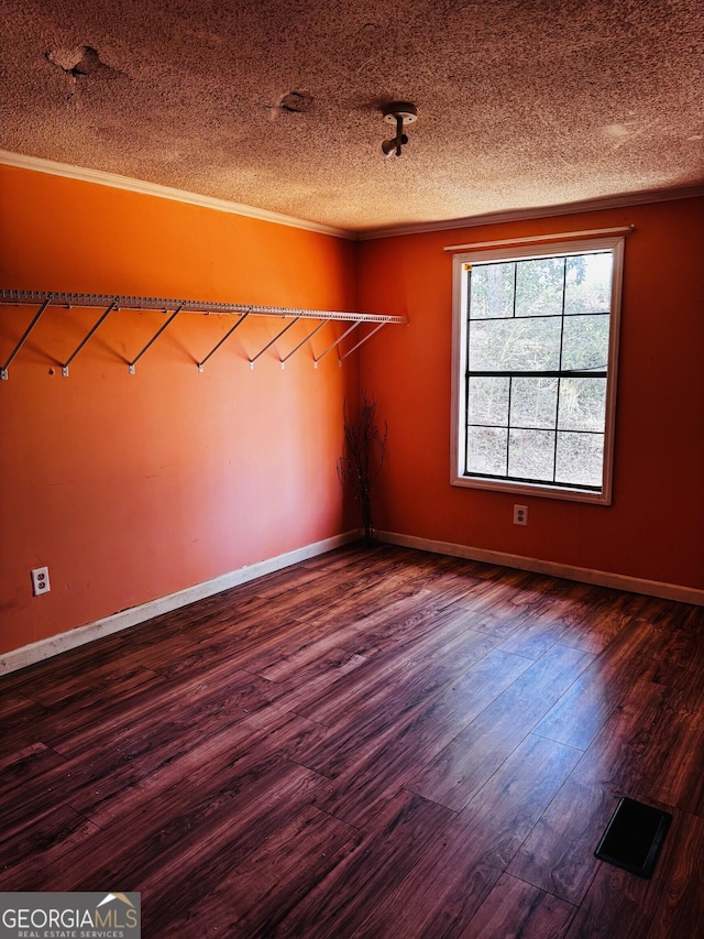 spare room featuring a textured ceiling, ornamental molding, dark wood-type flooring, and baseboards