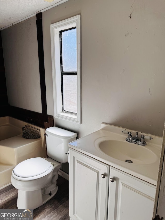 half bath featuring toilet, a wealth of natural light, wood finished floors, and vanity