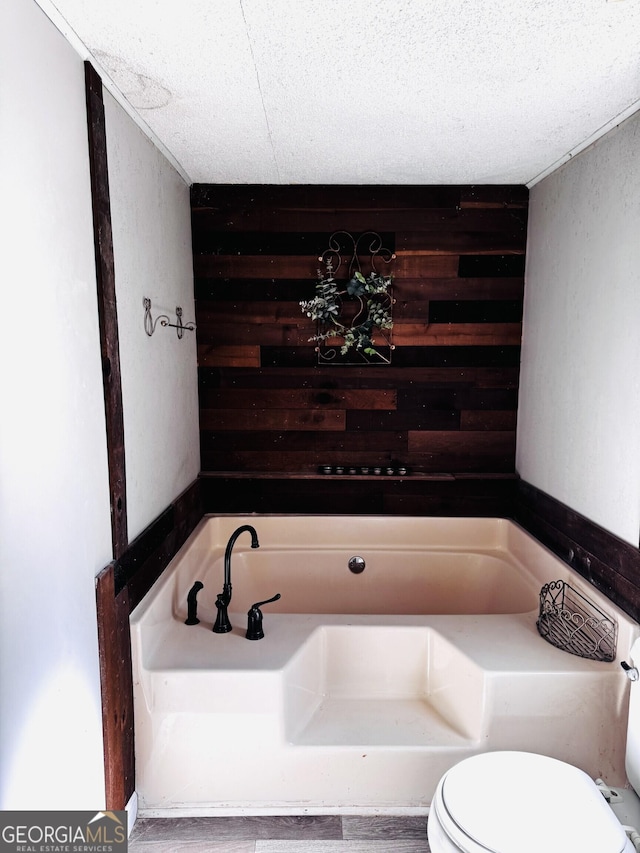 bathroom with toilet, a garden tub, and wood walls