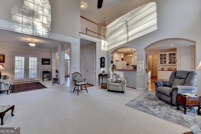 living room with arched walkways, a high ceiling, an inviting chandelier, ornamental molding, and light carpet