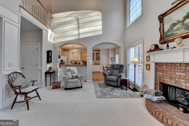 living room featuring arched walkways, a brick fireplace, carpet flooring, and a wealth of natural light