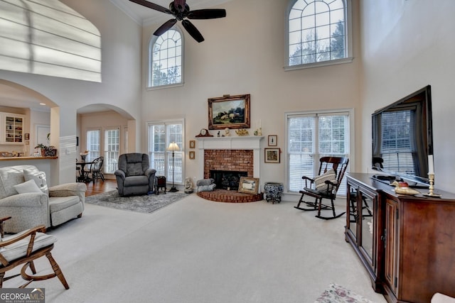 carpeted living room with arched walkways, ceiling fan, a fireplace, and crown molding