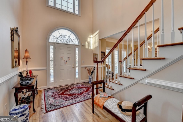 foyer entrance featuring stairs, a high ceiling, wood finished floors, and a healthy amount of sunlight