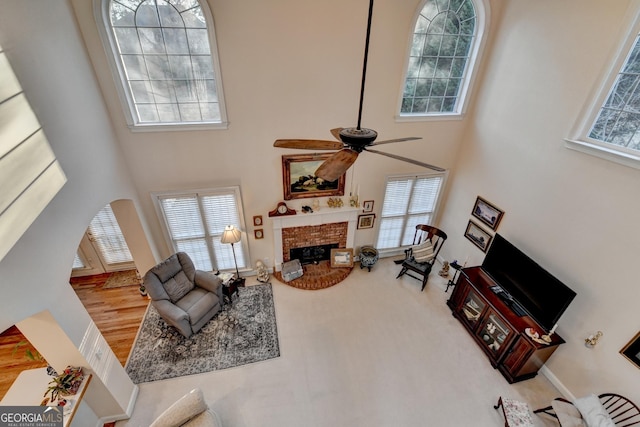 living room featuring arched walkways, a high ceiling, a brick fireplace, and a ceiling fan