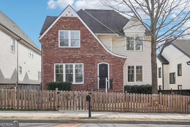 view of front of property with a fenced front yard, roof with shingles, and brick siding