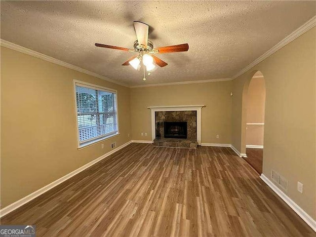 unfurnished living room featuring arched walkways, a stone fireplace, wood finished floors, a ceiling fan, and baseboards