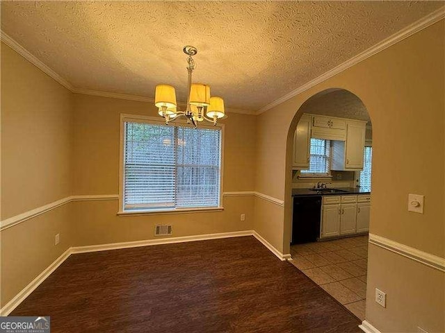 unfurnished dining area featuring a healthy amount of sunlight, crown molding, arched walkways, and wood finished floors