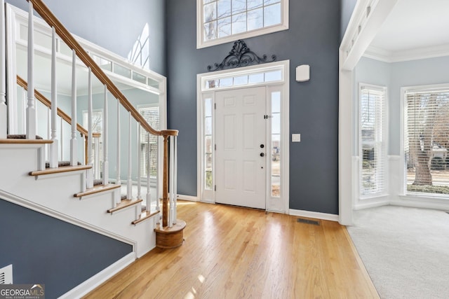 foyer entrance with crown molding, a towering ceiling, baseboards, and wood finished floors