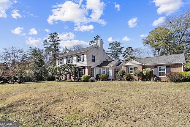 colonial house with brick siding, a chimney, and a front yard