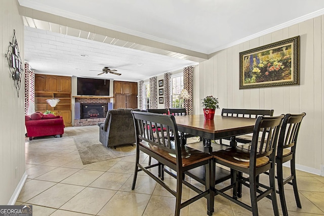 dining room featuring baseboards, a ceiling fan, ornamental molding, a brick fireplace, and light tile patterned flooring