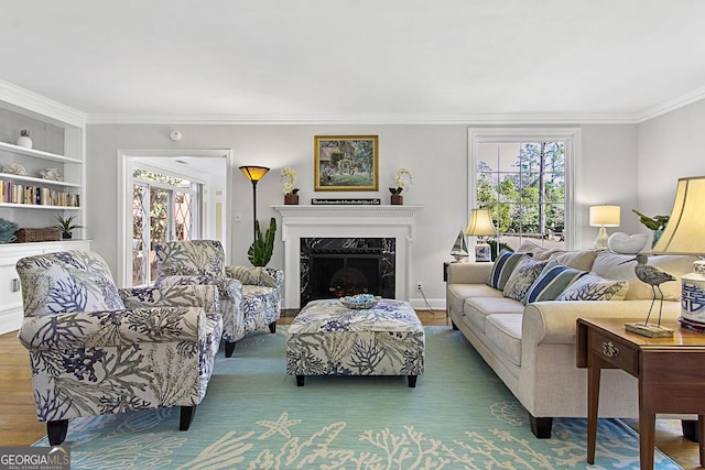 living area with baseboards, built in features, wood finished floors, crown molding, and a fireplace