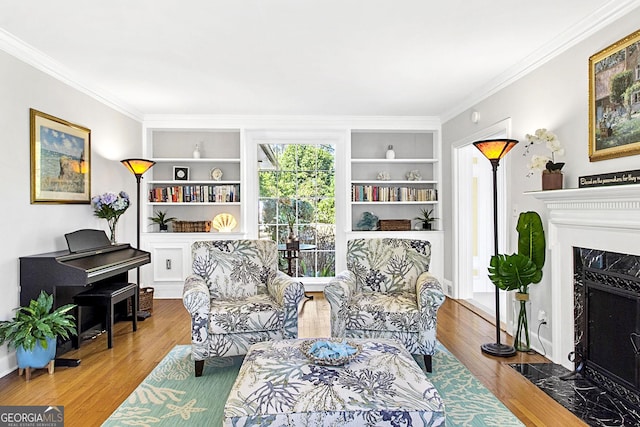 sitting room featuring built in shelves, crown molding, a premium fireplace, and wood finished floors