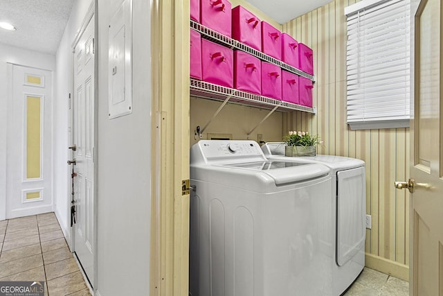 clothes washing area with light tile patterned floors, washing machine and dryer, a textured ceiling, laundry area, and electric panel