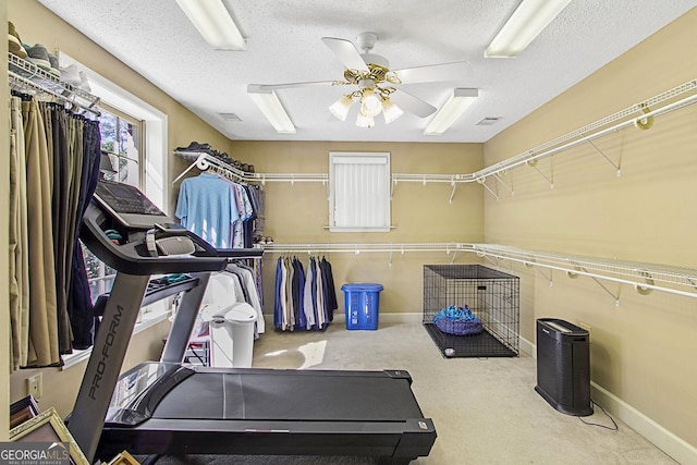 exercise room with a textured ceiling, carpet flooring, a ceiling fan, and baseboards