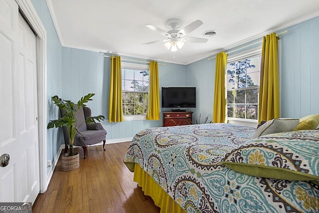 bedroom with ceiling fan, wood finished floors, visible vents, ornamental molding, and a closet