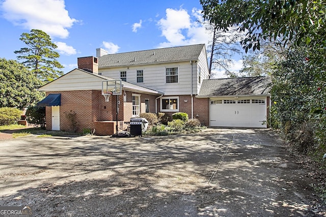 rear view of property with a garage, concrete driveway, brick siding, and a chimney