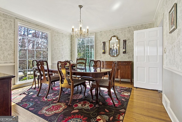 dining space featuring a wainscoted wall, a notable chandelier, ornamental molding, light wood-style floors, and wallpapered walls