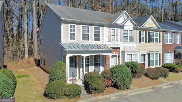 townhome / multi-family property with a standing seam roof, covered porch, brick siding, and metal roof