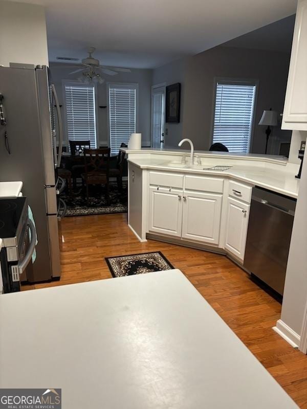 kitchen with appliances with stainless steel finishes, white cabinets, a peninsula, and wood finished floors