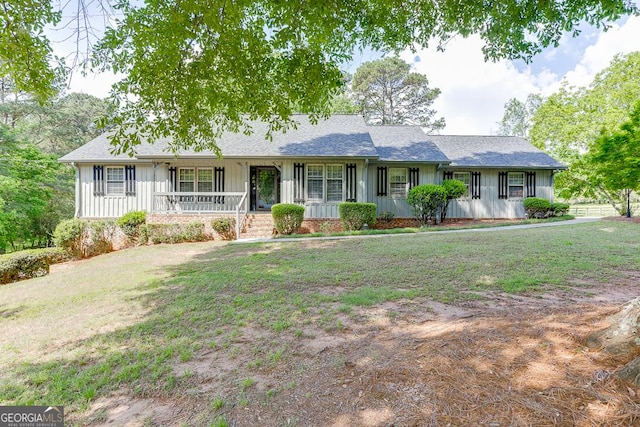 ranch-style home with board and batten siding, covered porch, a front yard, and roof with shingles