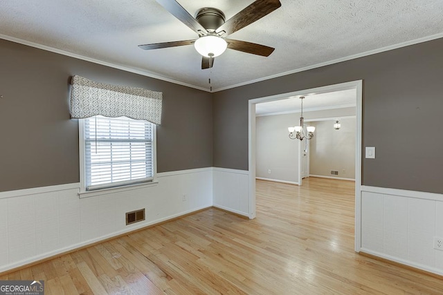 unfurnished room featuring a wainscoted wall, ceiling fan, a chandelier, light wood-style floors, and ornamental molding