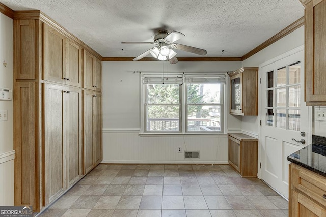 kitchen featuring ceiling fan, wainscoting, a textured ceiling, dark stone counters, and ornamental molding