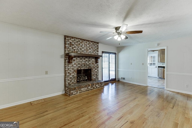 unfurnished living room with ceiling fan, wood finished floors, a textured ceiling, a fireplace, and baseboards