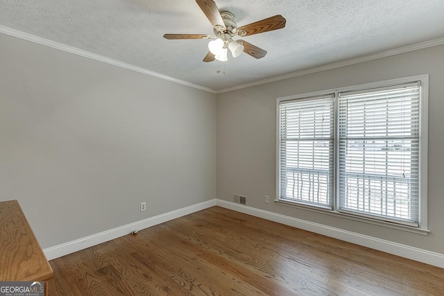spare room featuring wood finished floors, baseboards, a ceiling fan, ornamental molding, and a textured ceiling