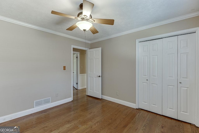 unfurnished bedroom with wood finished floors, baseboards, a closet, ornamental molding, and a ceiling fan