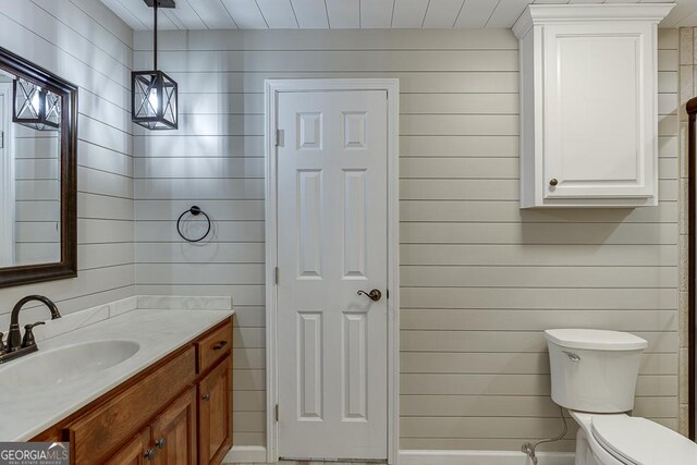 bathroom featuring wood walls, vanity, and toilet