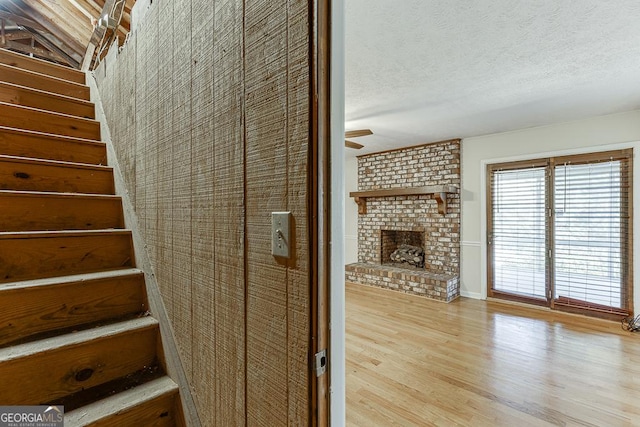 stairs featuring a fireplace, wood finished floors, ceiling fan, and a textured ceiling
