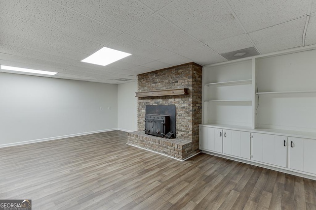 unfurnished living room with a drop ceiling, wood finished floors, and baseboards