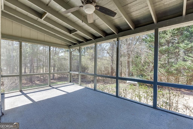 unfurnished sunroom featuring a ceiling fan and view of wooded area