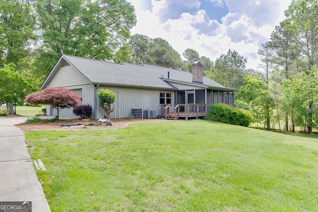 back of house featuring a sunroom, a chimney, a yard, and central AC