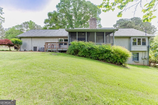 rear view of property featuring a chimney, a sunroom, a lawn, and a deck