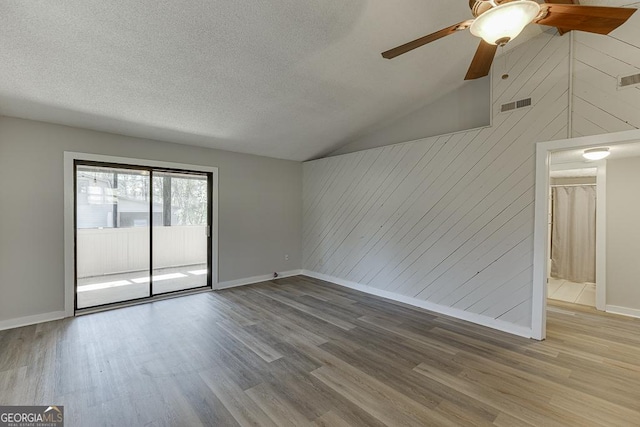 spare room with wood walls, wood finished floors, a ceiling fan, baseboards, and a textured ceiling