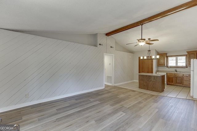 unfurnished living room featuring a ceiling fan, light wood-style floors, wood walls, a sink, and baseboards