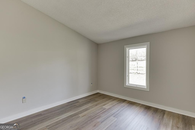 spare room featuring wood finished floors, a textured ceiling, and baseboards