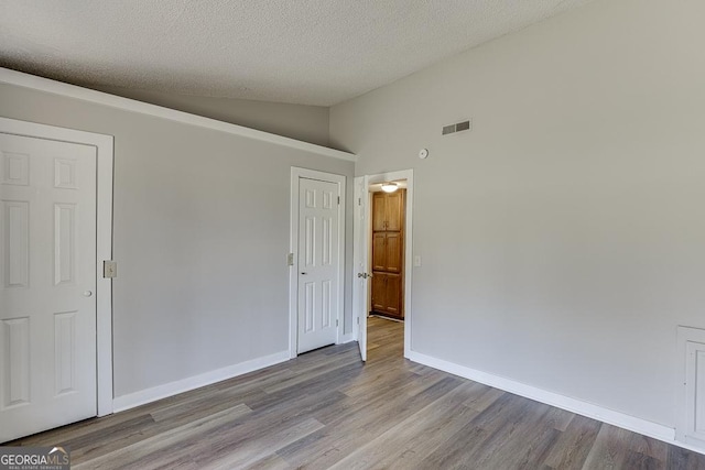 empty room featuring lofted ceiling, wood finished floors, a textured ceiling, and baseboards