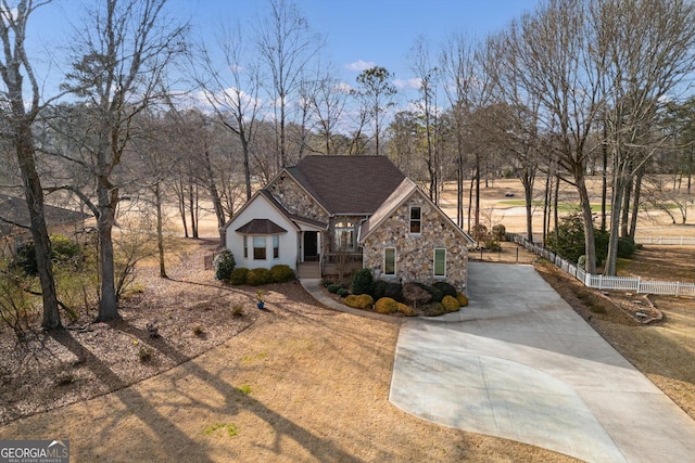 view of front of property with stone siding, a porch, fence, and driveway