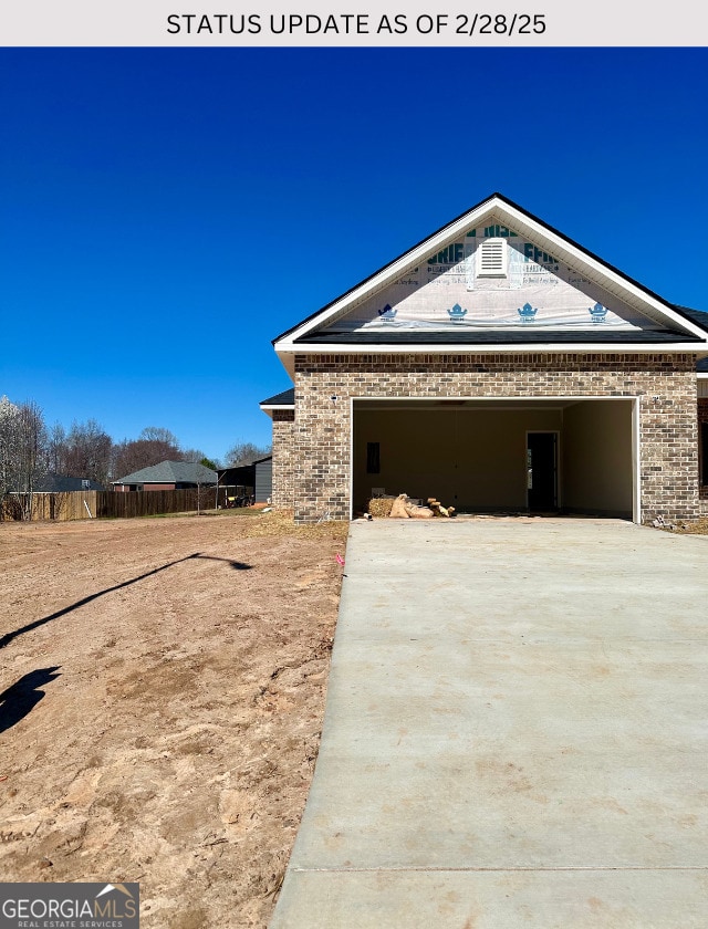 view of home's exterior featuring brick siding, driveway, an attached garage, and fence