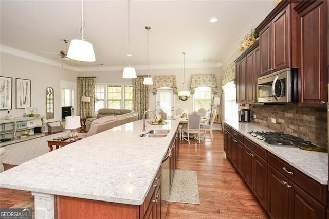 kitchen featuring appliances with stainless steel finishes, a sink, a large island with sink, and crown molding