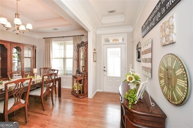 foyer entrance featuring a tray ceiling, light wood finished floors, and an inviting chandelier